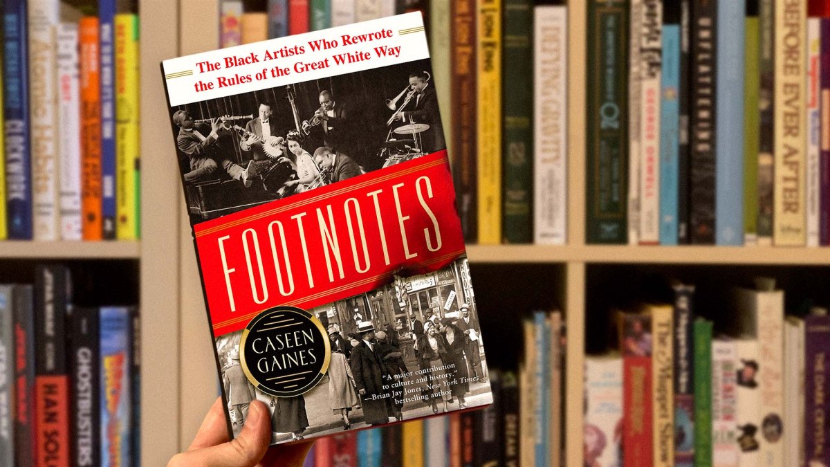 The cover of ‘Footnotes: The Black Artists Who Rewrote The Rules Of The Great White Way’ by author and historian Caseen Gaines features two old photos, one showing the all-black musicians of the Broadway show ‘Shuffle Along’ playing their instruments, the other a street bustling with black passers-by.