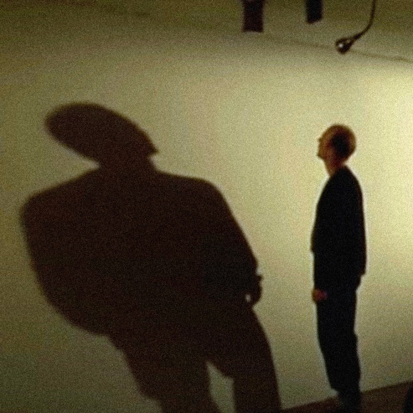A screenshot of the movie Pollock, showing Ed Harris as Jackson Pollock casting. A stark shadow on a huge, wall-sized, and empty canvas.